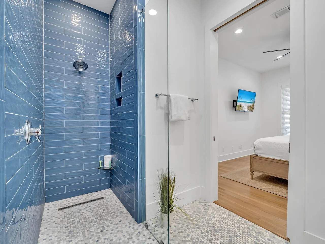 A modern bathroom with blue-tiled walls, a glass shower enclosure, a white sink, and a wooden floor.