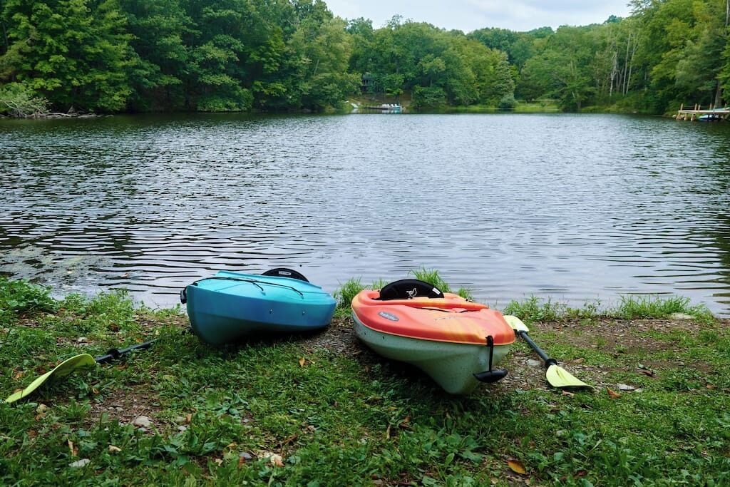 Two kayaks on a grassy lakeside with a forested backdrop.