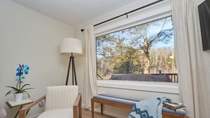 Ett rum med ett stort fönster, en stol, en bänk, en lampa och en krukväxt.
