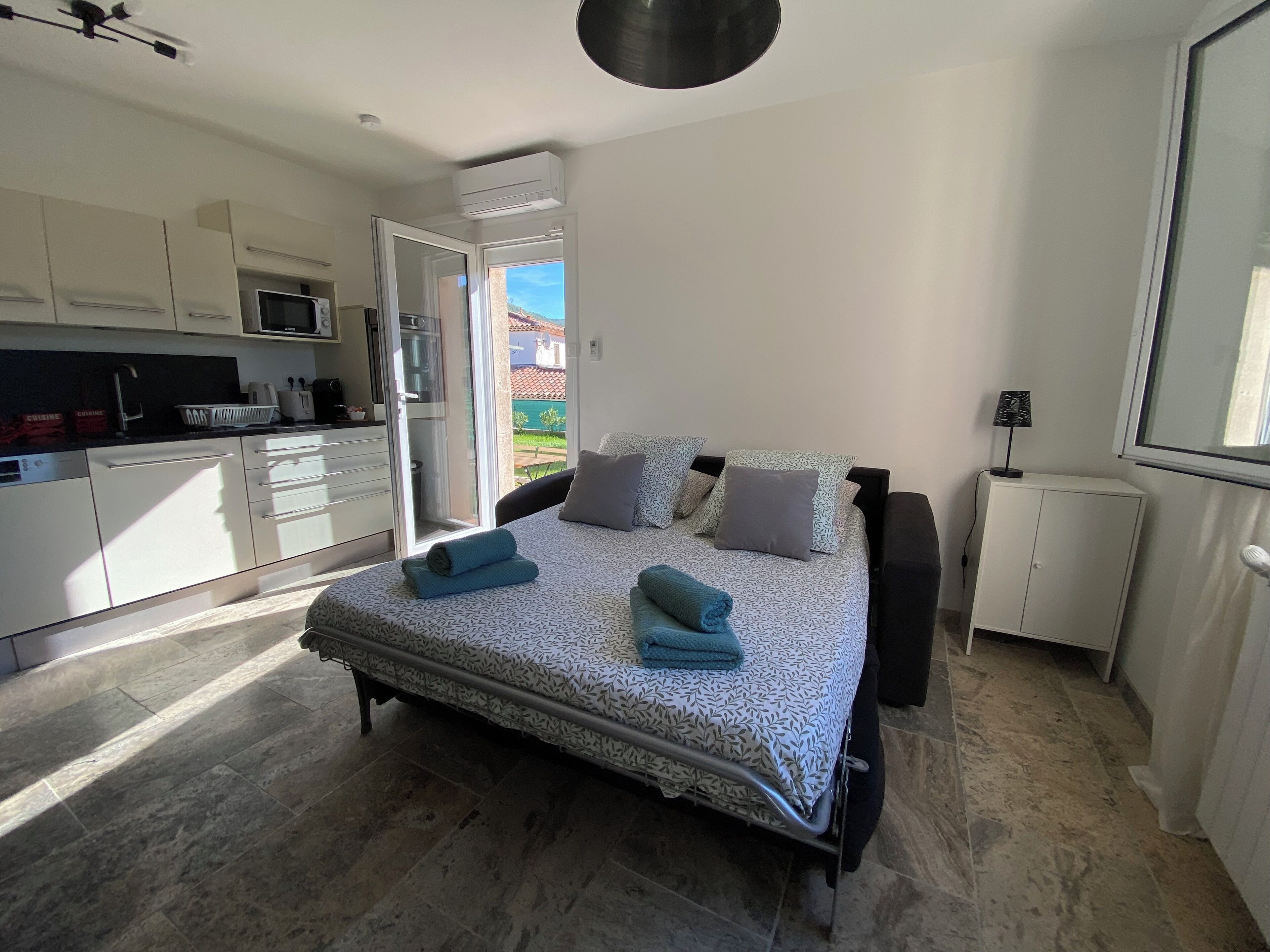 A bedroom with a bed, pillows, a bedside table, a lamp, and a view of the outside.