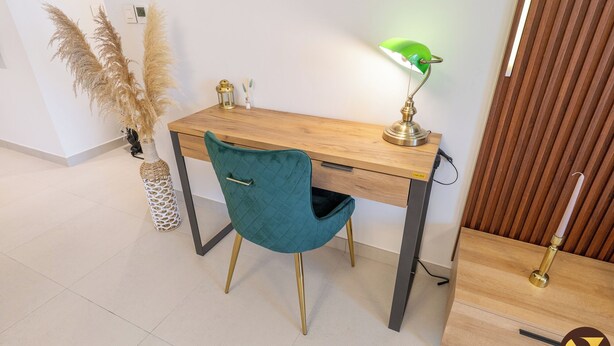 Een modern bureau met een blauwgroene stoel, een groene bureaulamp en decoratieve planten.
