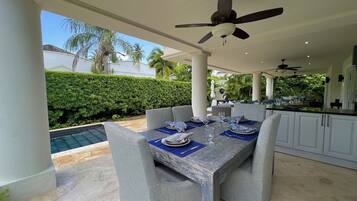 An outdoor dining area with a pool, covered patio, and kitchen area.