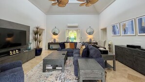 Een ruime woonkamer met een grote flatscreen-tv, twee plafondventilatoren, een zithoek, een salontafel en een eethoek.