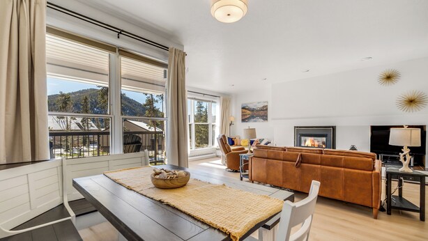 A modern living room with a dining area, large windows, a fireplace, and a view of the outdoors. - Mountain Comfort Steps From the Action (Keystone)