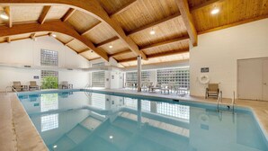 An indoor swimming pool with wooden beams, clear glass windows, and a tiled floor. - Mountain Comfort Steps From the Action (Keystone)