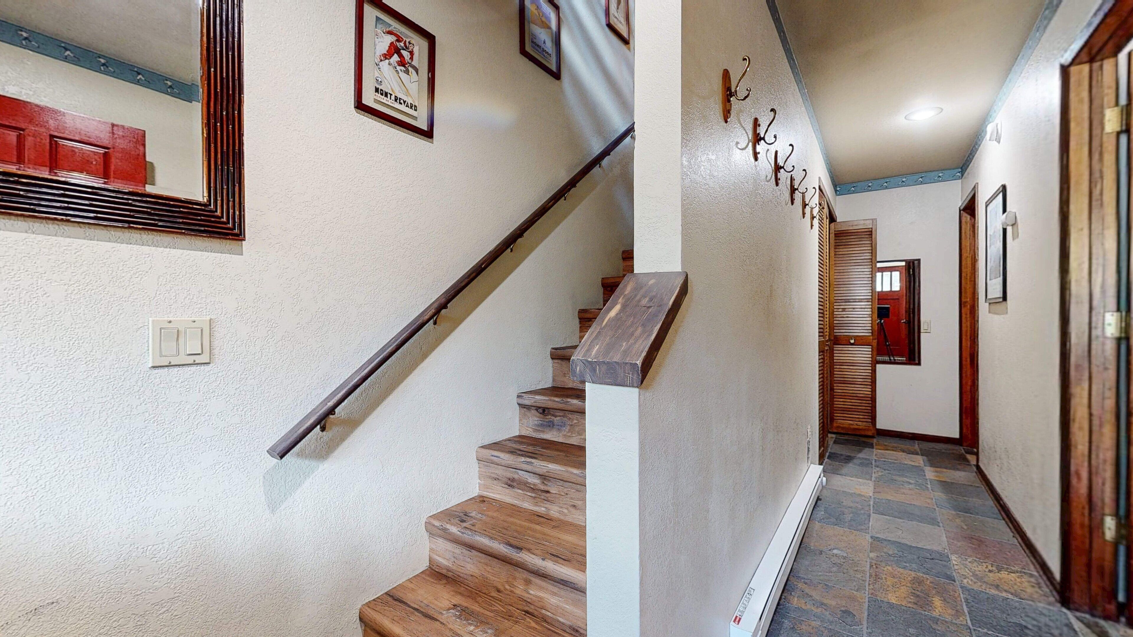 Un escalier avec des marches en bois et une rampe métallique, menant à une porte dotée d’un cadre en bois.