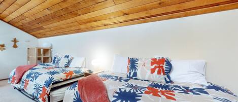 Une chambre avec un plafond en bois, un lit recouvert d’une literie à motifs floraux, une table de chevet et une petite table de nuit.