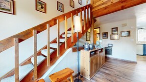 A wooden staircase with a white handrail, a wooden bench at the bottom, and a kitchen area with cabinets and a countertop. - Mammoth Sierra Townhomes #25 3 Bedroom Condo (Mammoth Lakes)