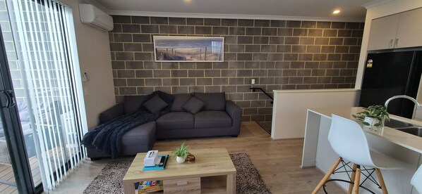 A modern living space with a grey sofa, a coffee table with a plant, and a kitchen area with a white countertop and sink. - 5 minutes walk to the beach! Alkimos Coastal 3 Bedroom Townhouse (Alkimos)