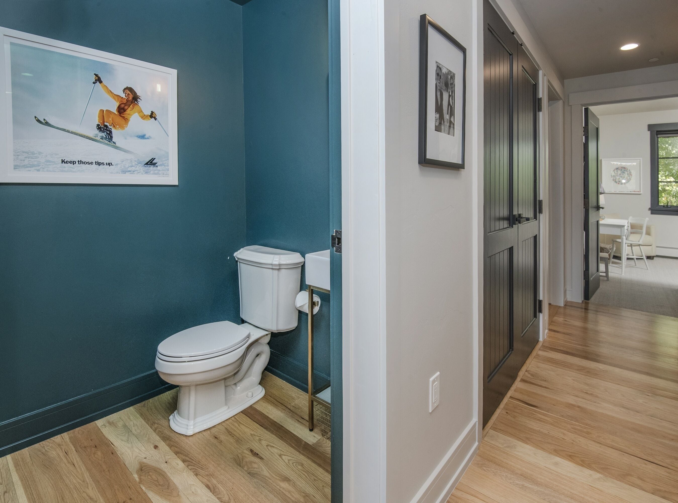 A modern bathroom with a toilet, a framed picture on the wall, and a wooden floor.