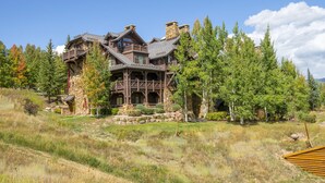 A large, multi-story lodge with a stone facade and wooden balconies, surrounded by a forested landscape.