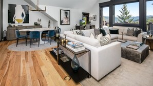 A modern living room with a white sofa, a dining table, and a chandelier.
