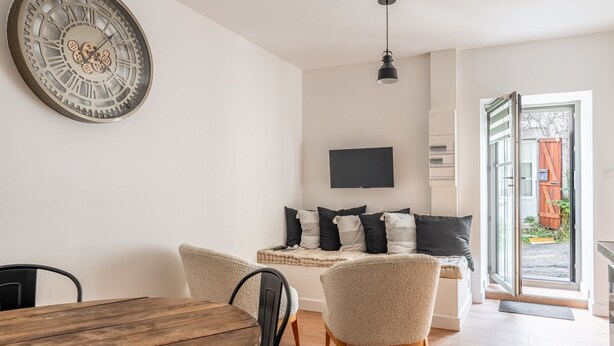 A modern living room with a wooden dining table, two armchairs, a sofa with black and white cushions, a mounted TV, and a large wall clock. - Holiday Home 'L'écrin De La Sèvre' with Wi-Fi (Cugand)