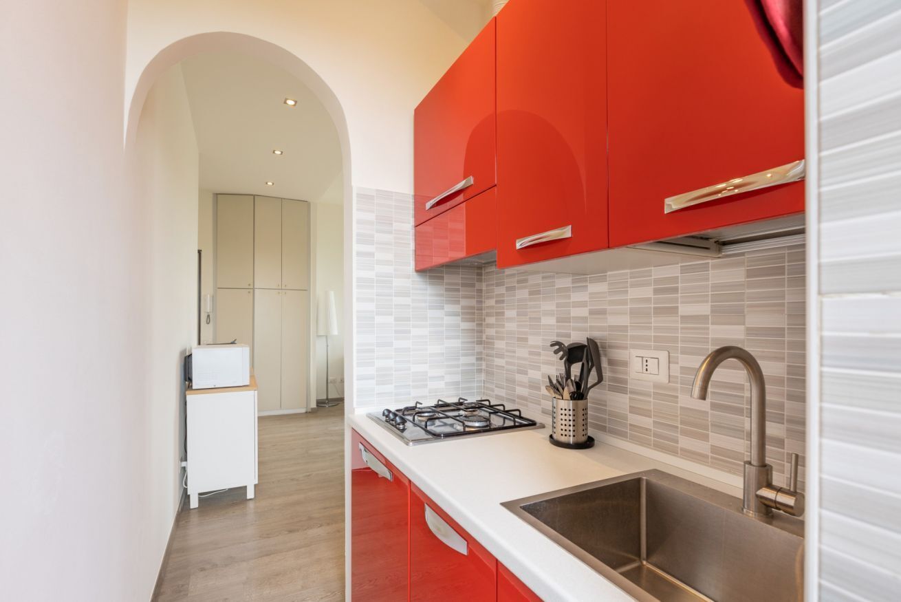 A modern kitchen with red cabinets, a stainless steel sink, and a tiled backsplash.