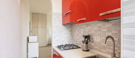 A modern kitchen with red cabinets, a stainless steel sink, and a tiled backsplash.