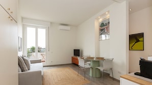 Una sala moderna con un sofá, una mesa de comedor con sillas, una mesa de centro y un televisor. Hay una ventana con vistas al exterior.