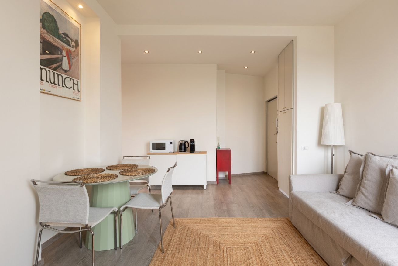 Una sala de estar moderna con sofá, una mesa de comedor con sillas, un área de cocina con microondas y un armario rojo.