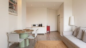 Una sala de estar moderna con sofá, una mesa de comedor con sillas, un área de cocina con microondas y un armario rojo.