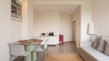 Una sala de estar moderna con sofá, una mesa de comedor con sillas, un área de cocina con microondas y un armario rojo.