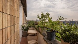 Un balcón con mesa y sillas de madera, plantas en macetas y vistas a la ciudad.