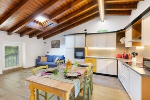 A modern kitchen with white cabinets, a dining area with a wooden table and chairs, and a blue sofa in the living area.