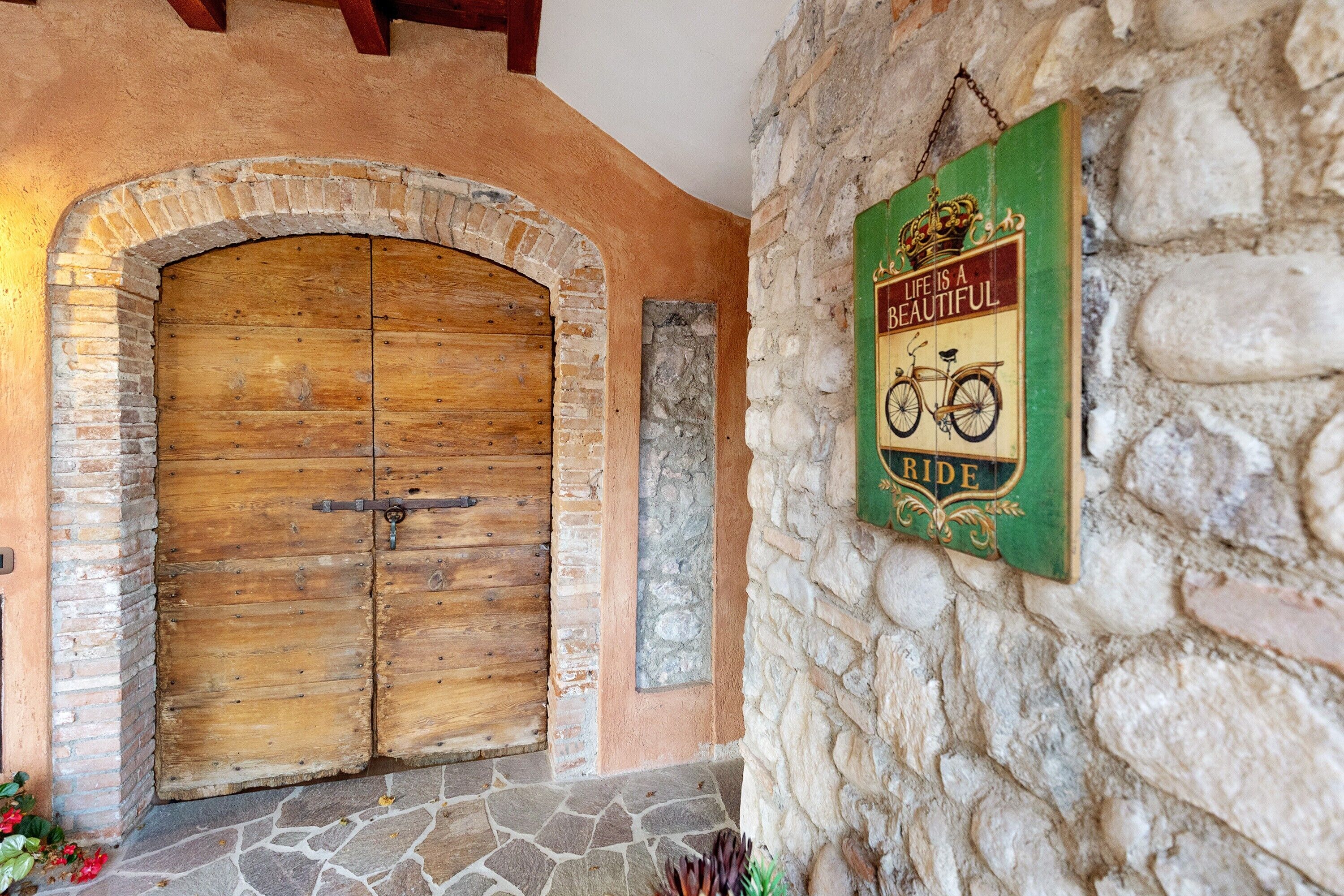 A rustic wooden door with a metal latch, a stone wall, and a green sign with a bicycle and crown emblem.