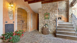A stone-floored entrance with a wooden door, a stone wall with a sign, and a staircase. - Apartment 'Il Borgo Ulivo' with Lake View, Wi-Fi and Air Conditioning (Castelletto)
