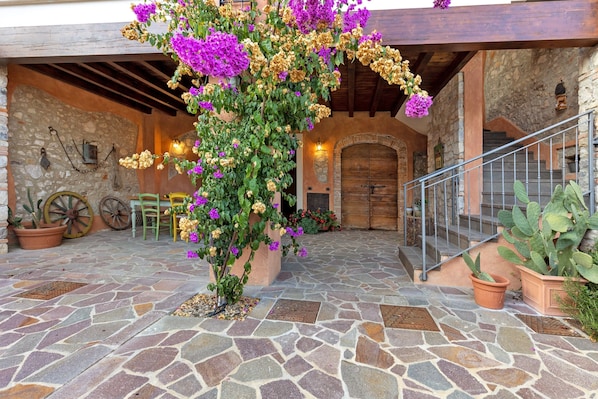 A stone-floored courtyard with a wooden staircase, potted plants, and a rustic stone wall.