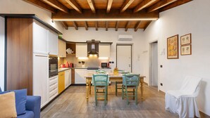 A modern kitchen with wooden beams, a dining area with chairs, and a sofa. - Apartment 'Il Borgo Ulivo' with Lake View, Wi-Fi and Air Conditioning (Castelletto)