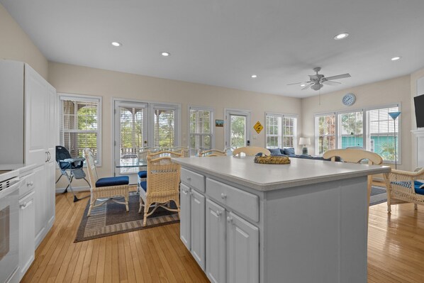A spacious kitchen with white cabinets, a large island, and a dining area with wicker chairs and a blue cushion.