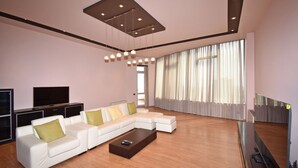 A modern living room with a white sectional sofa, a flat-screen TV, and a large window with sheer curtains.