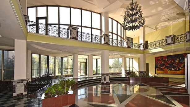 A spacious lobby with a high ceiling, large windows, and a central staircase.