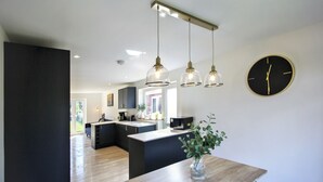 Una cocina moderna con iluminación colgante, una isla central y un reloj en la pared.