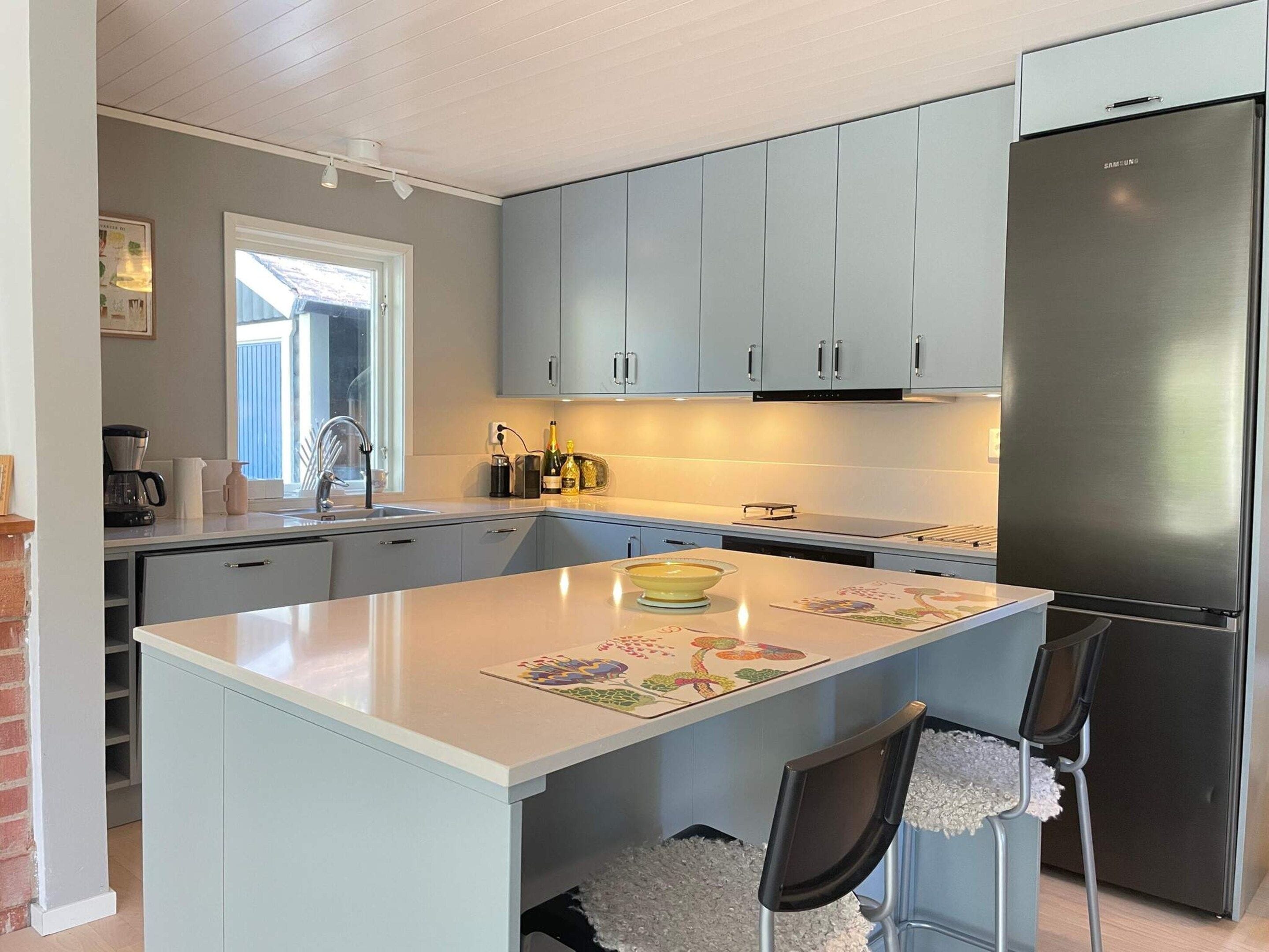A modern kitchen with grey cabinets, a stainless steel refrigerator, and a central island with chairs.