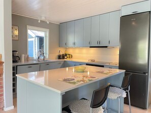 A modern kitchen with grey cabinets, a stainless steel refrigerator, and a central island with chairs. - 5 Star Holiday Home in Ystad (Ystad)
