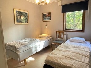 Ein Zimmer mit zwei Einzelbetten, einem Sessel, einem Tisch und zwei gerahmten Bildern an der Wand.