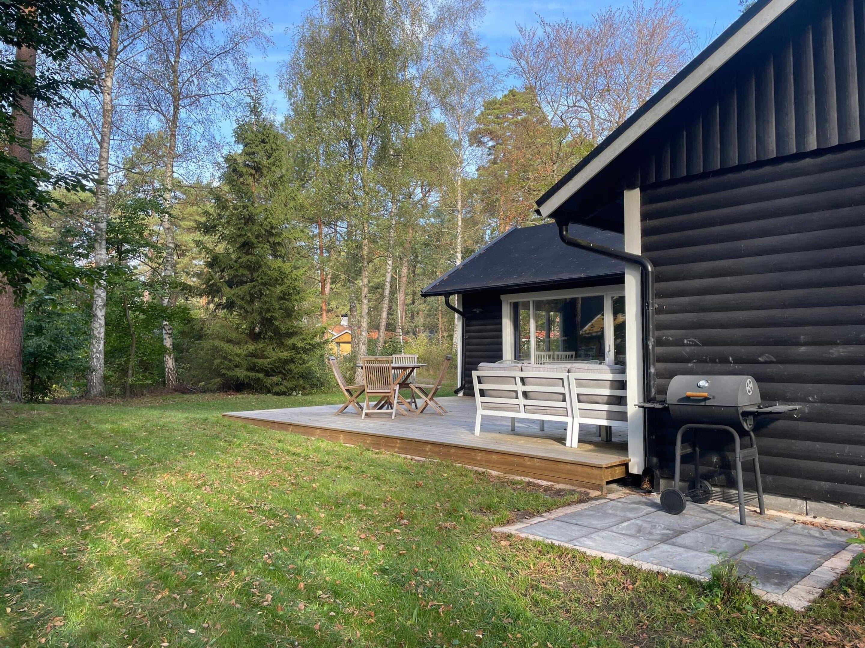A cabin with a deck, outdoor seating, and a grill.