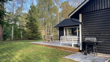 A cabin with a deck, outdoor seating, and a grill.