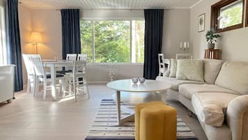 Uma sala de estar moderna com um sofá branco, uma mesa de centro redonda e uma área de jantar com cadeiras brancas.