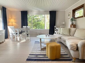 Un salon moderne avec un canapé blanc, une table basse ronde et un coin repas avec des chaises blanches.