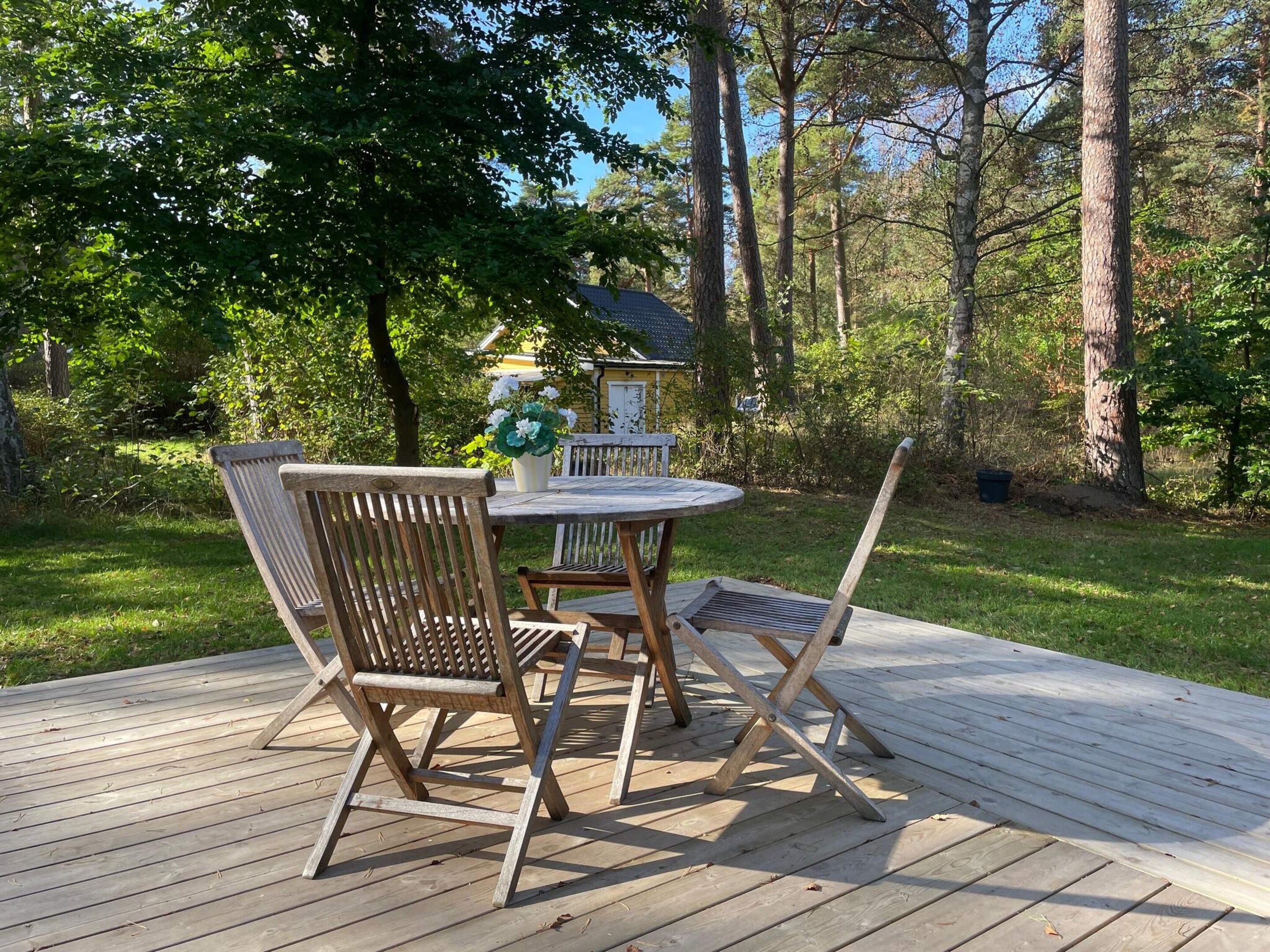 Una terraza de madera con una mesa redonda y cuatro sillas.