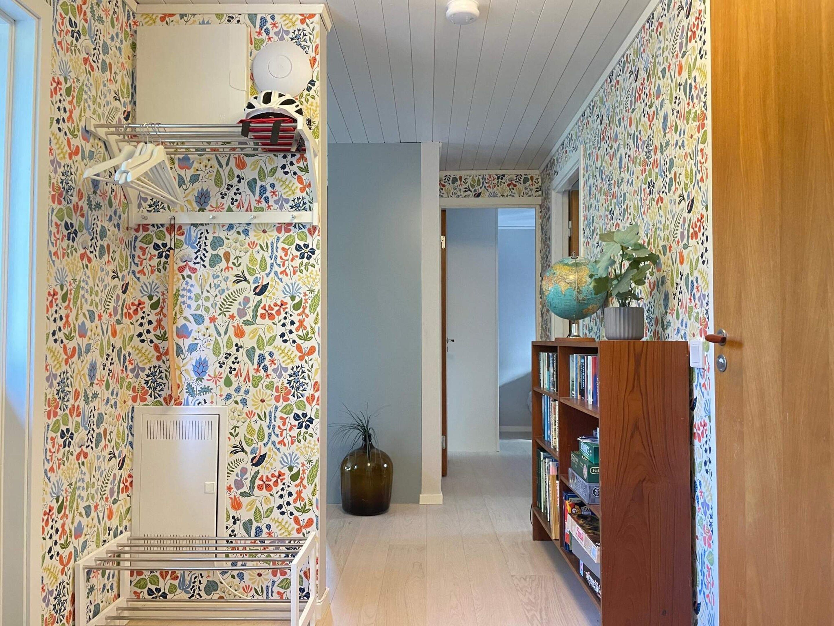 A hallway with patterned wallpaper, a globe on a shelf, and a wooden door.