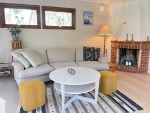 A living room with a sofa, a round table, a fireplace, and a window with a view of trees. - 5 Star Holiday Home in Ystad (Ystad)