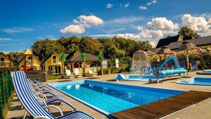 Ein Poolbereich mit mehreren Schwimmbecken, Liegestühlen und einer Wasserrutsche.