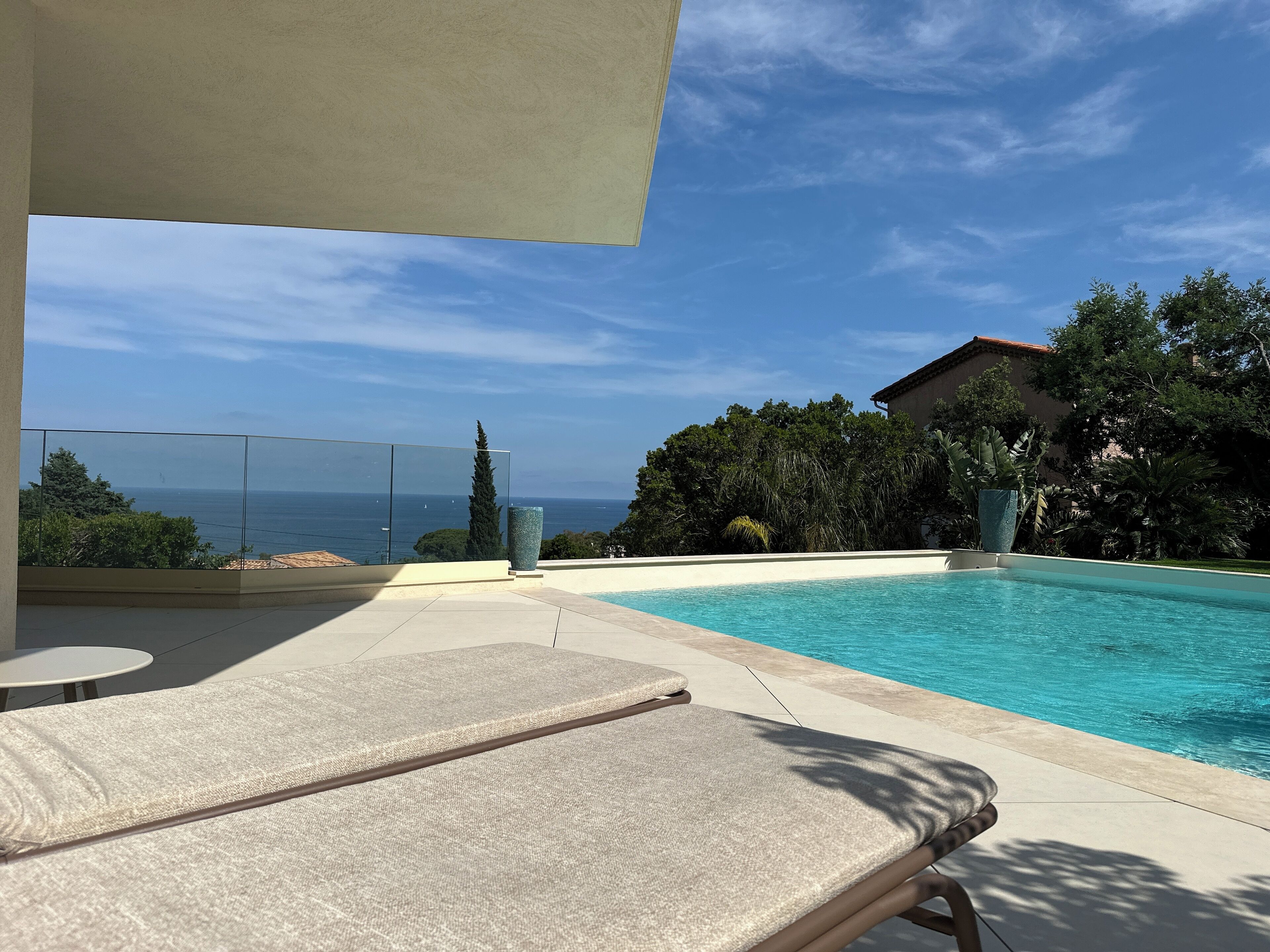 A poolside area with lounge chairs, a clear view of the sea, and a large decorative vase.