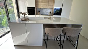 A modern kitchen with a large island, pendant lights, and a view of greenery outside. - Villa Les Issambres, infinity pool, sea view (Roquebrune-sur-Argens)