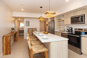 Une cuisine moderne dotée d’un îlot central, d’appareils électroménagers en acier inoxydable et d’un banc en bois servant de coin repas.