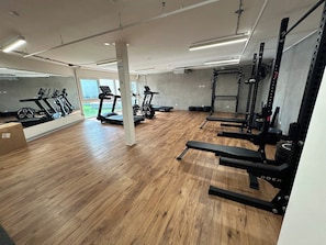 Ein Fitnessraum mit Trainingsgeräten, Holzboden und einem großen Spiegel.