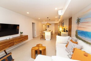 A modern living room with a flat-screen TV, wooden furniture, a sofa with cushions, and a painting of a beach scene. - Luxury Ocean Front Condo (Jaco Beach)