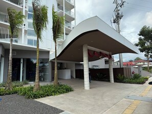 A modern building with a covered entrance, palm trees, and a clear sky. - Luxury Ocean Front Condo (Jaco Beach)